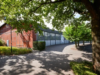 Ringlokschuppen Ruhr, Mülheim an der Ruhr <p>Rotes Backsteingebäude mit großflächigen Fenstern, umgeben von schattenspendenden Bäumen.</p>
