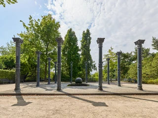 Ringlokschuppen Ruhr, Mülheim an der Ruhr Steinkreis mit hohen Säulen im Freien, umgeben von Bäumen und hellem Himmel mit Wolken.