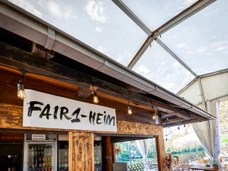 FAIR1-HEiM in der Tomate, Mülheim an der Ruhr <p>Im Bild ist ein Café unter einem Zeltpavillon zu sehen, mit einem Schild "FAIR1-HEIM".</p>