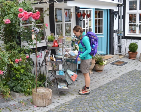 Tecklenburg_Innenstadt_Julia_Bohlken.jpg Eine Wanderin mit lila Rucksack betrachtet einen Flohmarktstand in einer gepflasterten Altstadtgasse.
