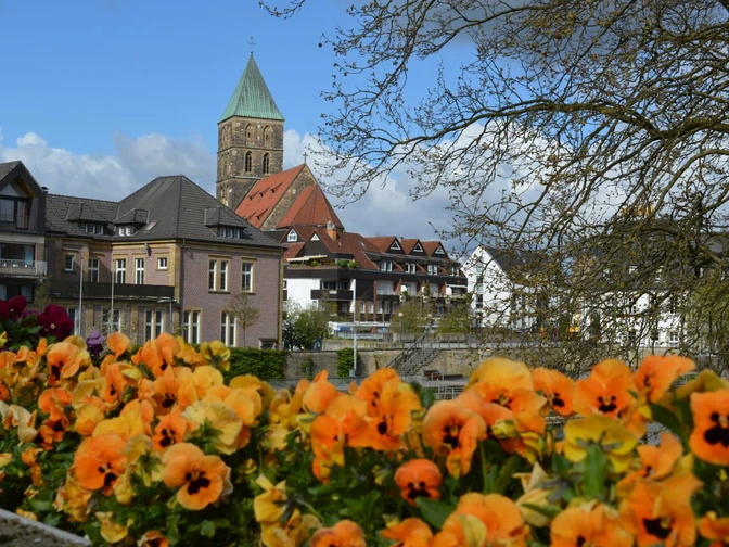 Rheine_Emsufer_Foto_Teutoburger Wald Tourismus_I Bohlken_1600.jpg Blick auf blühende orangefarbene Blumen mit einer beeindruckenden Kirche im Hintergrund, leicht bewölkter Himmel.