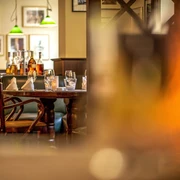 Restaurant Tilia im Hotel Lindenhof Gemütlich gedeckter Tisch in einem Restaurant mit Holzmöbeln, Gläsern, Flaschen und grünen Hängelampen im Hintergrund, warme Atmosphäre.