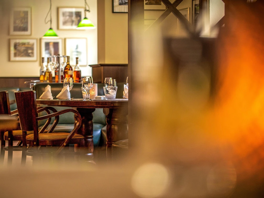 Restaurant Tilia in the Hotel Lindenhof Gemütlich gedeckter Tisch in einem Restaurant mit Holzmöbeln, Gläsern, Flaschen und grünen Hängelampen im Hintergrund, warme Atmosphäre.