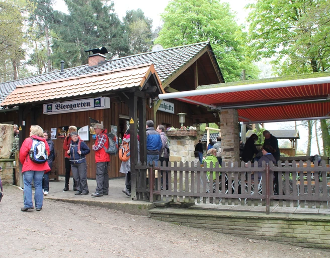 Dörenther Klippen_Almhütte_Teutoburger Wald Tourismus.JPG Eine Gruppe Wanderer versammelt sich vor einer Almhütte mit Biergarten im Teutoburger Wald.