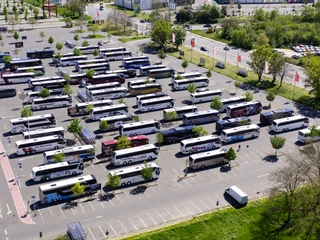 Buslogistik I Ein Parkplatz voller Reisebusse, in Reihen geparkt, von oben gesehen. Bäume und Gebäude im Hintergrund.A parking lot full of coaches, parked in rows, seen from above. Trees and buildings in the background.
