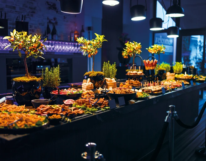 Impressionen Events Dunkler Eventraum, in der Mitte steht ein Tisch mit Catering BuffetDark event room, in the middle is a table with a catering buffet