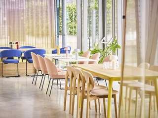 DSC06713.jpg Lichtdurchfluteter Raum mit bodentiefen Fenstern und drei Gruppentischen mit bunten StühlenLight-flooded room with floor-to-ceiling windows and three group tables with colorful chairs