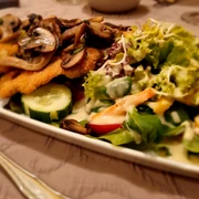 Holter_Krüstchen_CC_BY_SA_Teutoburger_Wald_Stadt_Schloss_Holte-Stukenbrock.jpg Panierte Schnitzel mit gebratenen Pilzen, angerichtet auf einem Teller neben frischem Salat.