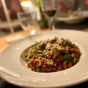 SpaghettiBolognese_CC_BY_SA_Teutoburger_Wald_Stadt_Schloss_Holte-Stukenbrock.jpg Ein Teller mit Spaghetti Bolognese, angerichtet mit Petersilie und Parmesan auf einem gedeckten Tisch.
