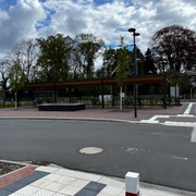 Überdachte Fahrradstellplätze am Bahnhof.jpg Überdachte Fahrradstellplätze am Bahnhof, mit modernen Strukturen, beleuchtet bei Tageslicht. Im Hintergrund sind Bäume und ein Gebäude erkennbar.
