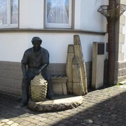 Korbmacher-Museum Dalhausen Eine Korbmacherstatue aus Bronze vor dem Museum, mit geflochtenen Körben und typischen Arbeitsgeräten.