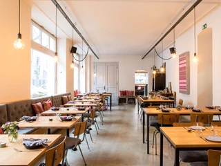 Tigermilch Gemütliches Restaurant mit Holzmöbeln, offener Beleuchtung und farbenfroher Kunst an den Wänden.Cozy restaurant featuring wooden furnishings, open lighting, and colorful artwork adorning the walls.