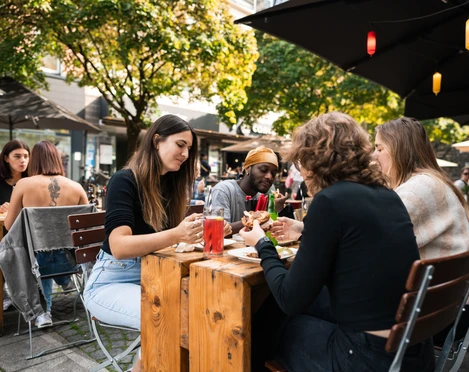 Freddy Schilling Eigelstein Junge Mensch essen Burger an einem Holztisch in der Außengastronomie.Young people eating burgers at a wooden table in an outdoor restaurant.