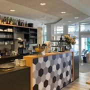 nostimo_3.jpg Moderner Gastronomietresen in Grautönen und Holzoptik und Regal mit Gläsern im Hintergrund