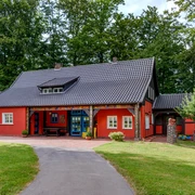 Teutoburger Wald / Museum Peter August Böckstiegel / Werther (Westf.) / Foto: M. Wallenfang Farbkräftiges rotes Haus im Fachwerkstil mit blau umrahmter Tür, umgeben von üppigem Grün.