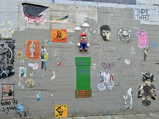 Wall of fame Eine bunte Wand mit kunstvollen Graffitis und Stickern, darunter ein Mario-Spielcharakter und verschiedene Pop-Art-Motive, erweckt urbane Kreativität zum Leben.A colorful wall adorned with artistic graffiti and stickers, including a Mario video game character and various pop-art motifs, bringing urban creativity to life.