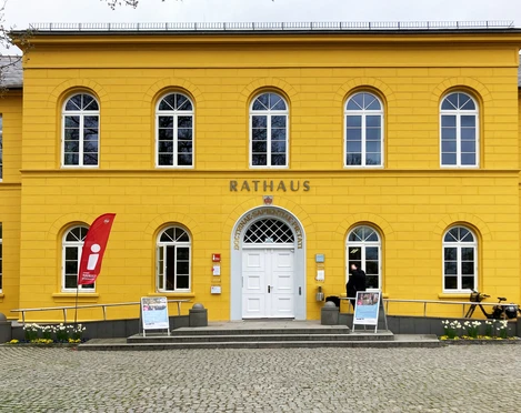 Ratzeburg_Rathaus_TouristInfo5_052024_Petra_Roemer.jpg Rathaus, gelbes Gebäude mit Aufsteller und Fahne für die Tourist-Information