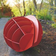 Harald a. Finke Modell Pflanzendenkmal-Chloroplast-Mitochondrium 2022.jpg Das Bild zeigt eine kunstvolle, rot bemalte Skulptur im Freien, die kugelförmig gestaltet ist und aus mehreren Segmenten besteht. Sie liegt auf einem gepflasterten Weg und wird von grüner Vegetation umrahmt.