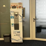 Trinkwasserspender im Rathaus_Manuela Baumhöfer.jpg Silberner Trinkwasserspender mit Bechern und Infomaterial im Eingangsbereich eines Büros.