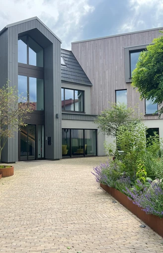 Ein modernes Gebäude mit großen Fenstern, umgeben von gepflegtem Grün und einer gepflasterten Einfahrt.