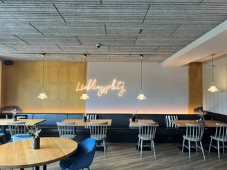 Ein modernes Café mit Holztischen, schwarzen Sitzbänken und dekorativen Deckenleuchten.