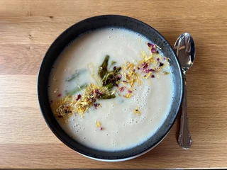 Eine cremige Spargelsuppe in einer dunklen Schüssel, dekoriert mit essbaren Blüten und Spargelstücken.