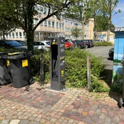 Graue ADAC-Service-Station für Fahrräder inmitten von Parkplatz, umgeben von Bäumen und Mülleimern.