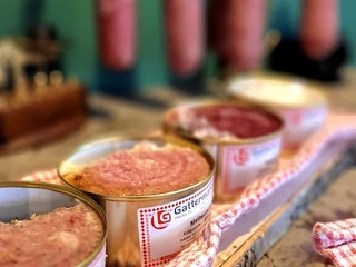 Kruegers_Frühstücksbuffet_Wurst_02.jpg Verschiedene Wurstsorten in Dosen auf Holztisch, im Hintergrund hängende Wurststangen.
