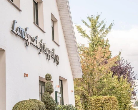 Außenansicht eines weißen Gebäudes mit dem Schriftzug "Landgasthof Stempferhof" und gepflegten Büschen.