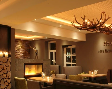 Gemütliche Restaurant-Innenansicht mit Kamin, modernen Sitzgruppen und dekorativer Hirschgeweih-Lampe.