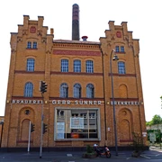 Brauwelt in Cologne-Kalk Historisches Brauereigebäude in Köln-Kalk mit markanter Ziegelfassade und großen Fenstern bei blauem Himmel.Historic brewery building in Cologne-Kalk with striking brick façade and large windows under a blue sky.