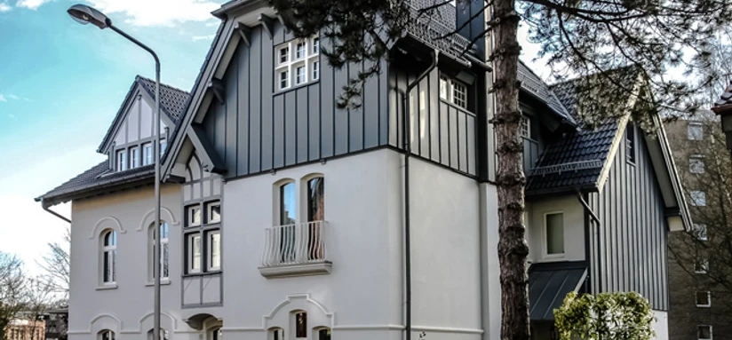 Fabrikantenvilla in Erkrath Eine prächtige Villa mit historischer Fassade und modernen Akzenten, umgeben von Bäumen und Zäunen.