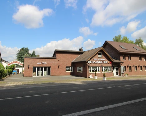 Hotel und Restaurant Haaner Hof Das Bild zeigt ein Backsteingebäude mit Restaurant Haaner Hof, umgeben von Bäumen und blauen Himmel.
