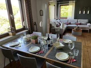 Wohnzimmer im Ferienhaus Brinker Bleibe in Velbert-Langenberg. Essbereich und Wohnzimmer mit gedecktem Tisch, Holzfußboden, heller Couch und Fenstern mit Ausblick.