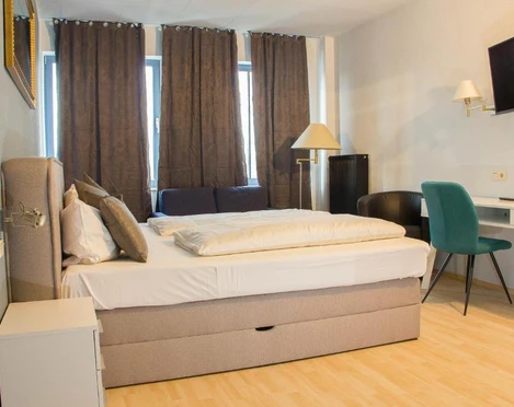 Hotelzimmer im Stargaze Forum Hotel in Hilden Helles Hotelzimmer mit Doppelbett, Schreibtisch, Stuhl, Wand-TV und großzügigen Fenstern mit Vorhängen.