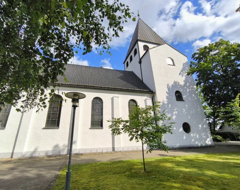 Die Herz-Jesu-Kirche in Hövelriege, weiß getüncht, mit Glockenturm und umliegenden Grünflächen.