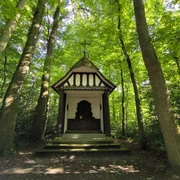 Eine kleine, weiße Kapelle mit Fachwerkelementen, umgeben von dichtem, grünem Wald.