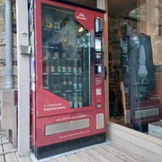 Proviantomat in Stolpen Roter Verkaufsautomat mit Snacks und Getränken, aufgestellt neben einer Steinmauer und einem Holzregal.