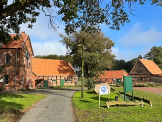 Noltesche Mühle Bruchhausen-Vilsen (5).jpg Historische Backsteinmühle in Bruchhausen-Vilsen mit Nebengebäuden und Sitzbereich unter Bäumen.
