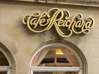 Cafe Reichard Außenansicht mit Blick durch das Schaufenster auf die Tortenvitrine. Darüber in golden geschwungener Schrift Cafe ReichardExterior view with a view of the cake display case through the shop window. Above it, in curved gold lettering, Cafe Reichard