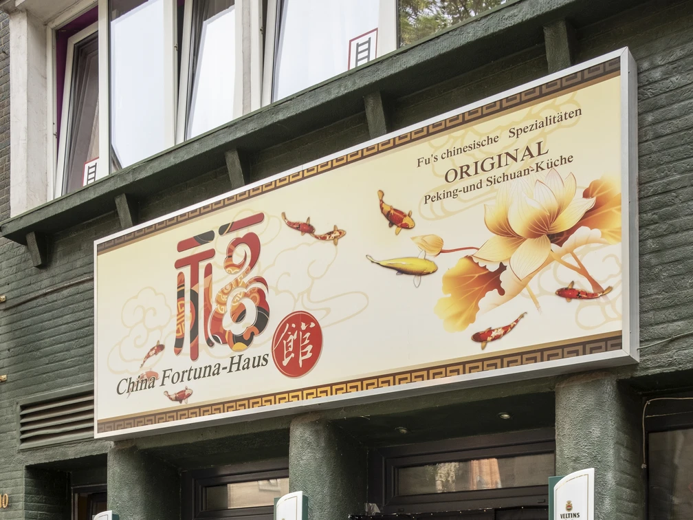 China Fortuna Haus Haupteingang zum Restaurant, darüber ein auffallend großes Schild mit Restaurantnamen und Floralen Details. Main entrance to the restaurant, with a remarkable large sign above it with the restaurant name and floral details.