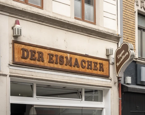 Der Eismacher Einladender Eingang einer modernen Eisdiele mit stilvoller Holzbeschilderung in urbanem Umfeld.Inviting entrance of a modern ice cream parlor with stylish wooden signage in an urban setting.