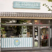 Die Eisdielerin Fröhliche beige Fassade mit hell blauem Schild aus Holzbrettern .Cheerful beige facade with a light blue sign made of wooden boards.