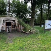 Plaggenhütte Nordloh mit Infotafel.jpg Eine traditionelle Plaggenhütte, neben einem Baum, mit Infotafel und Bank im Grünen.