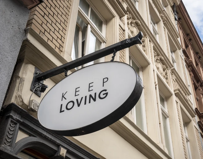 Keep Loving Ein ovales Schild mit der Aufschrift "Keep Loving" hängt an einem historischen Gebäude in der Stadt.An oval sign with the words "Keep Loving" hangs on a historic building in the city.