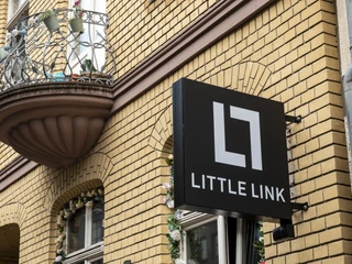 Bar Little Link An einer Fassade mit hellen Backsteinen hängt das Barschild im schlichten Design.The bar sign hangs in a simple design on a facade with light-colored bricks.