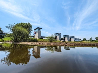 Petershagen Stauwehr spiegelt sich im ruhigen Wasser wider, umgeben von grüner Vegetation und blauem Himmel.
