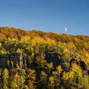 Great Winter Mountain in autumn Herbstliche Landschaft mit buntem Laubwald und Felsen im Vordergrund, Halbmond am klaren blauen Himmel.