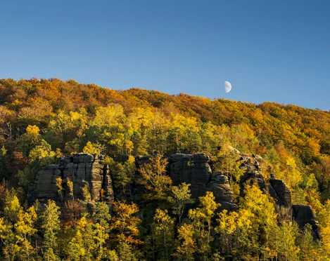 Großer Winterberg im Herbst Herbstliche Landschaft mit buntem Laubwald und Felsen im Vordergrund, Halbmond am klaren blauen Himmel.
