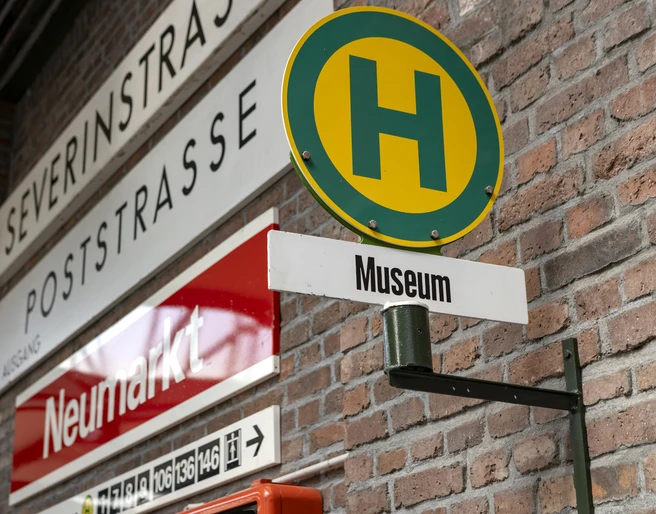 Thielenbruch Tram Museum Straßenschilder und ein Haltestellenschild „Museum“ an einer Ziegelmauer.Street signs and a "Museum" stop sign on a brick wall.